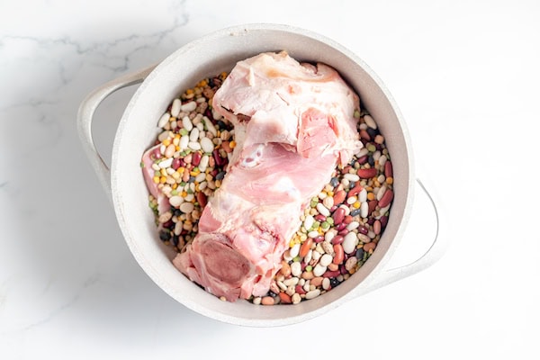 Image, taken from above, shows a large stock pot with hamhock and beans in it on a white counter top. 