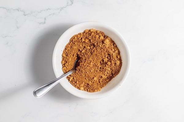 Image, taken from above, shows a small bowl of cinnamon brown sugar mixture for sourdough cinnamon rolls.