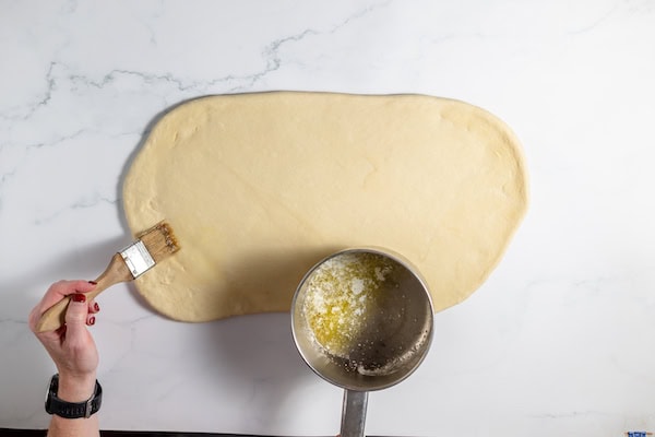 Image, taken from above,  shows a hand brushing rolled out dough with butter.