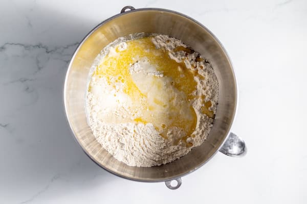 Image, taken from above, shows butter, milk, and sourdough starter added to dry ingredients in a large glass mixing bowl.