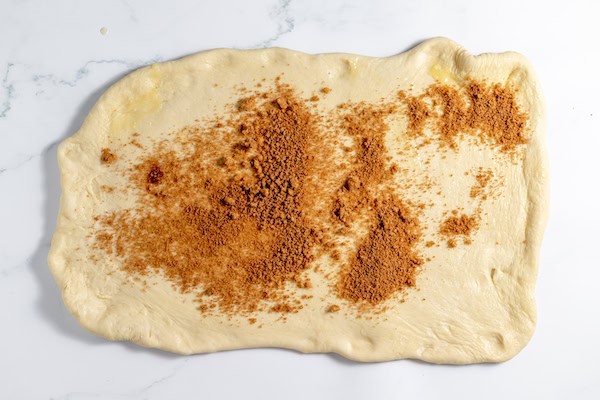 Image, taken from above, shows cinnamon sugar sprinkled on dough rolled out on a counter top.