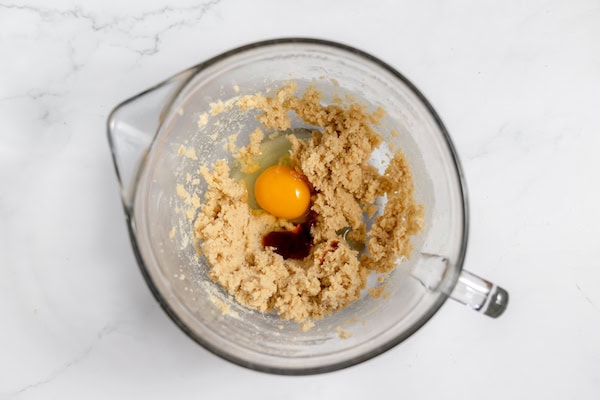 Image shows vanilla and egg added to butter and sugar mixture in a large mixing bowl.