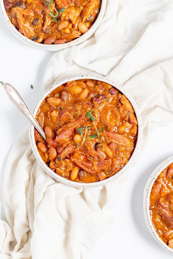 Image, taken from above, shows ham and 15 bean soup served in bowls with thyme on an off white tablecloth.