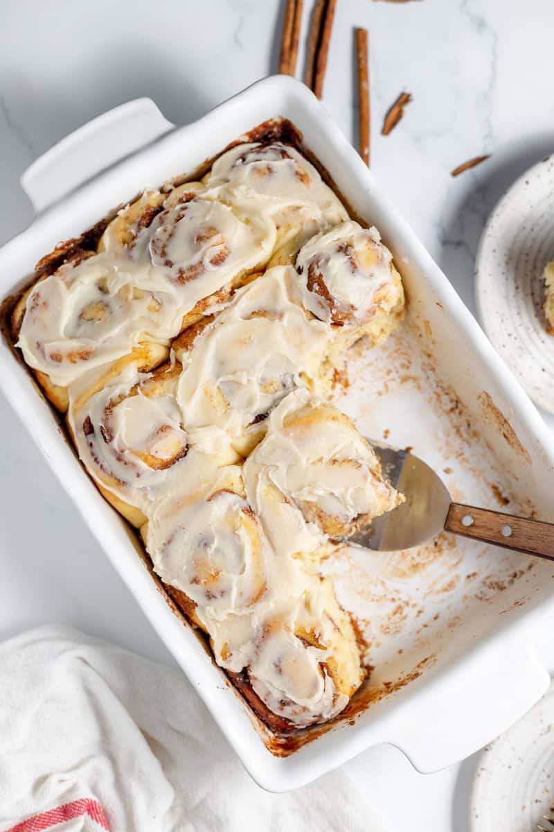 Image, taken from above, shows a pan of cinnamon rolls made with sourdough and iced with vanilla icing.