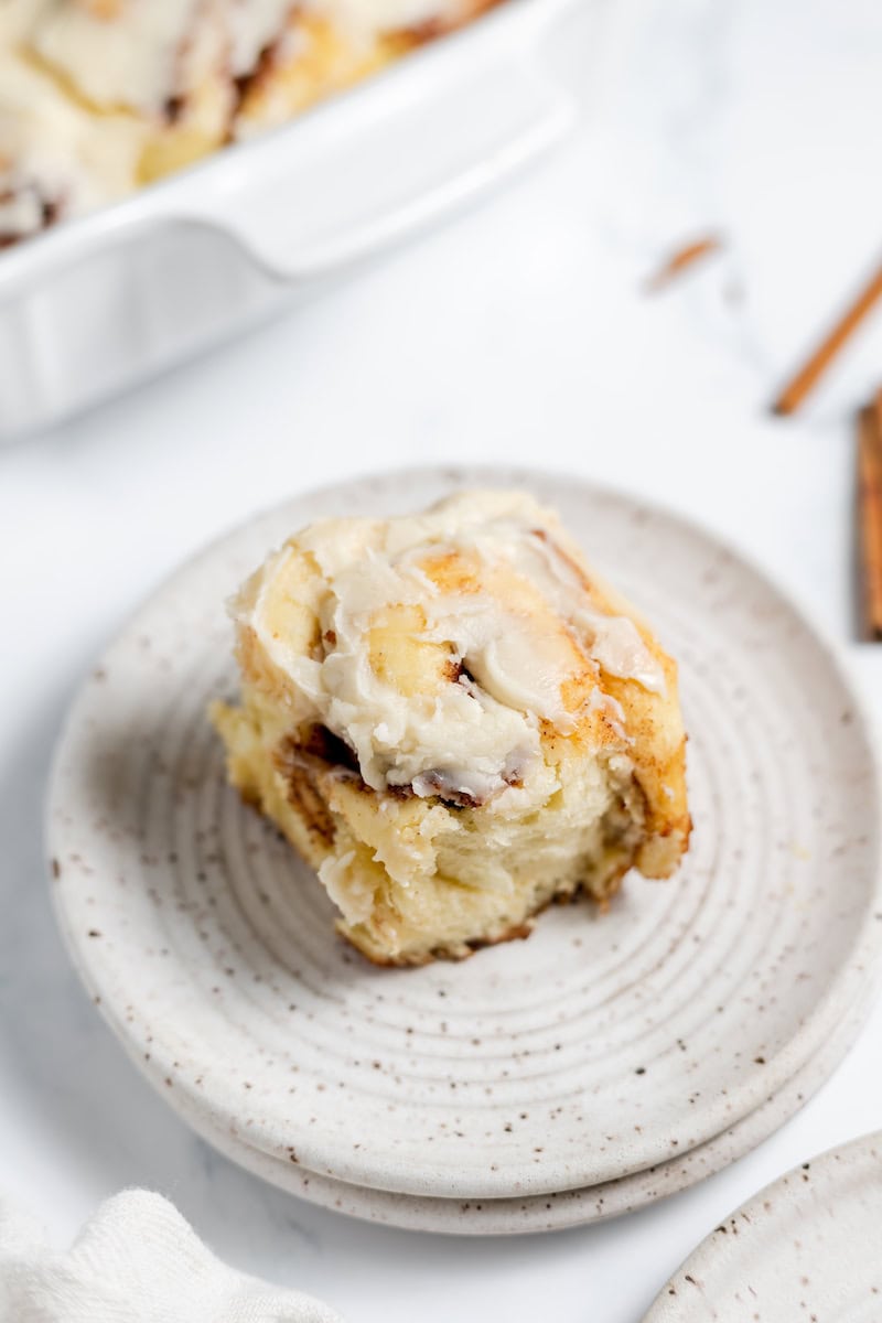 Image shows a close up of a plate with a frosted sourdough cinnamon roll on it.