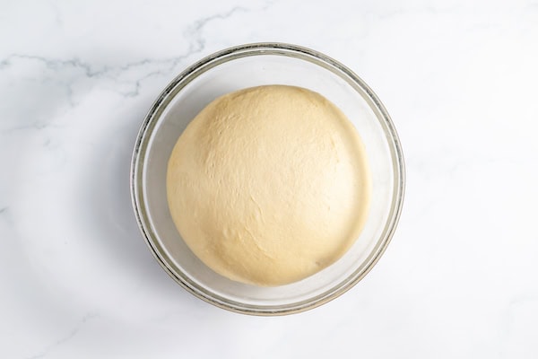Image, taken from above, shows the ball of dough in a glass bowl proofed and ready for rolling out.