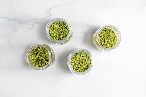 Image, taken from above shows several canning jars of split peas on a white counter.