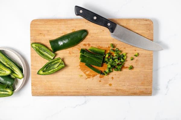 dicing jalapenos on a cutting board with a sharp knife