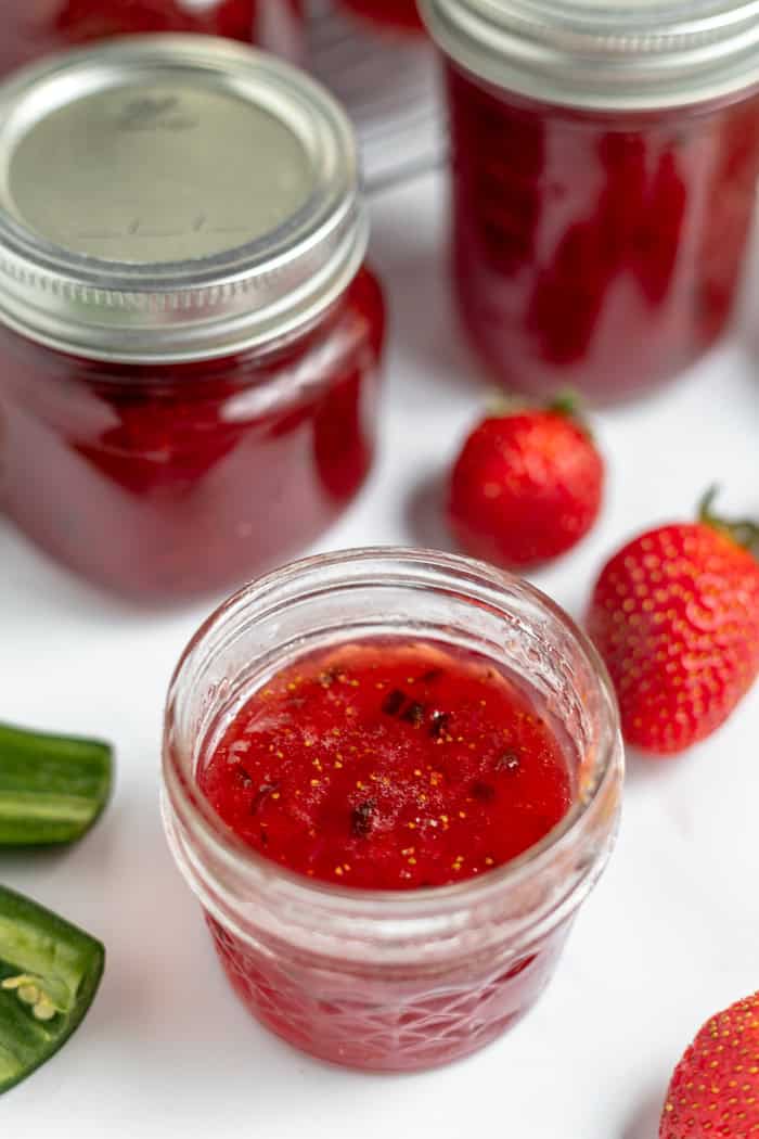 an open jar of strawberry jalapeño jam with strawberries and other jars around it