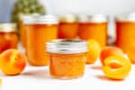 jars of apricot pineapple jam on a table with fruit