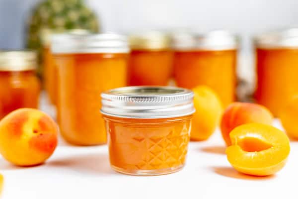 jars of apricot pineapple jam on a table with fruit