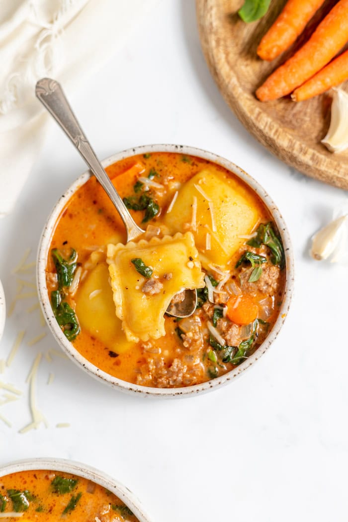 bowl of soup with ravioli, spinach, carrots, and tomatoes