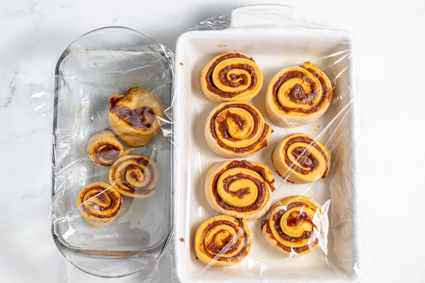 cinnamon rolls in pans, covered with plastic wrap